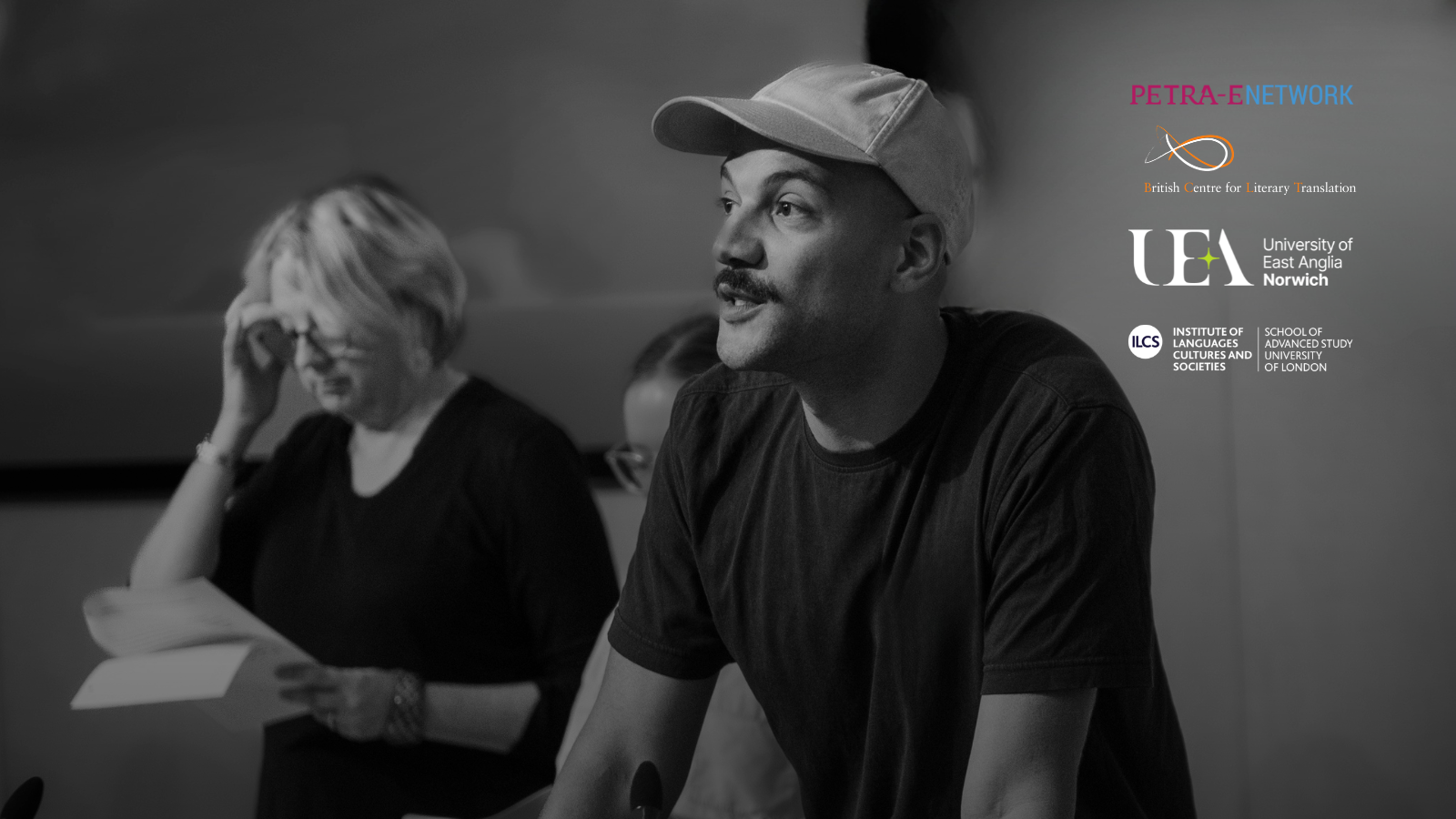 A black and white photo of a man in a cap speaking. In the background, a woman looks at papers. Logos for academic institutions are on the right.