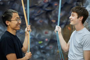 Two men at climbing wall smiling at each other.