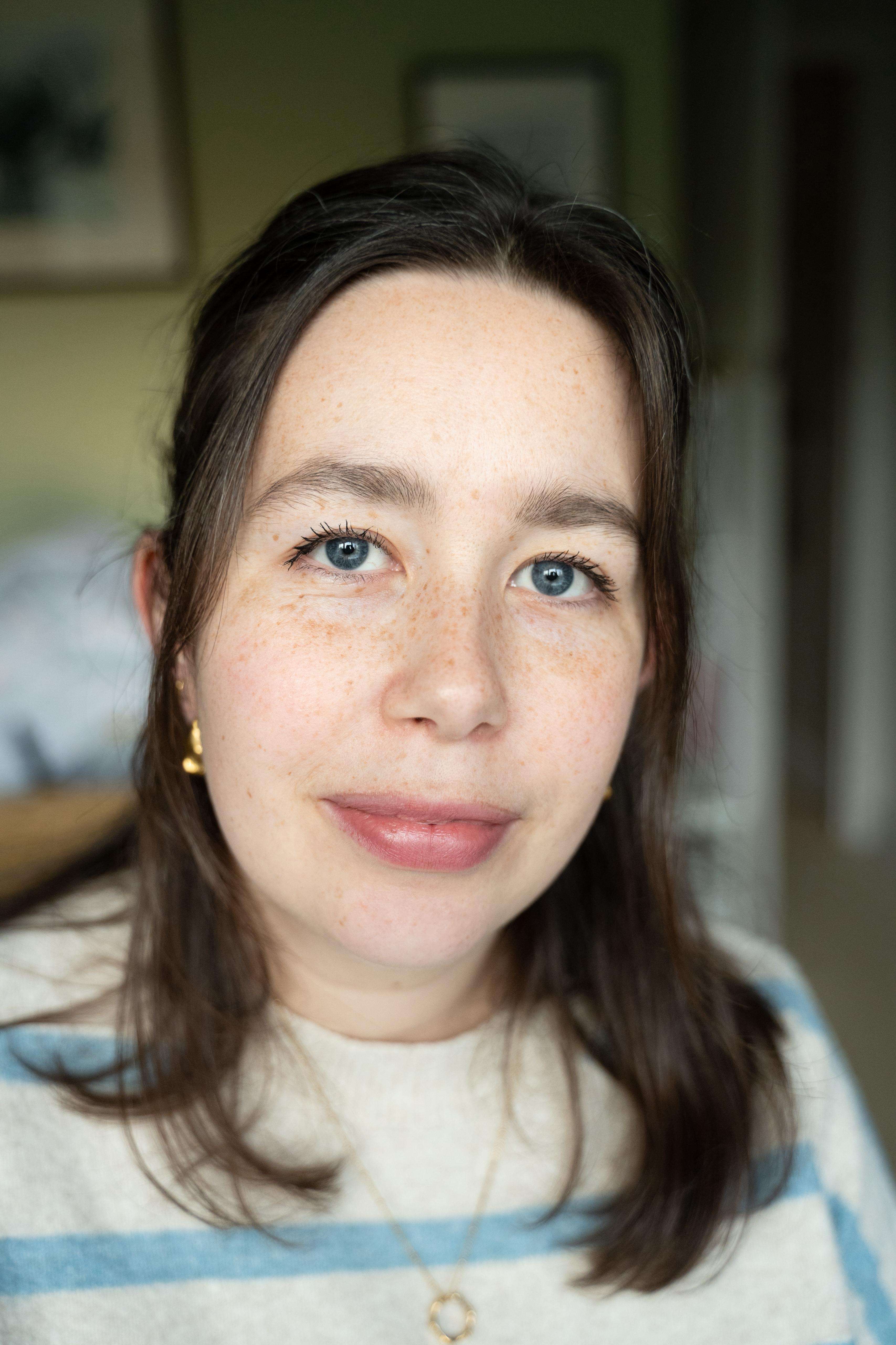A close-up portrait of a young woman with brown hair, bright blue eyes, and freckles, looking at the camera with a gentle expression.
