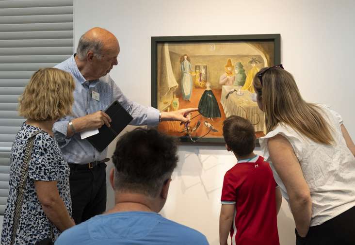 A Sainsbury Centre tour guide points at a painting whilst others watch on.