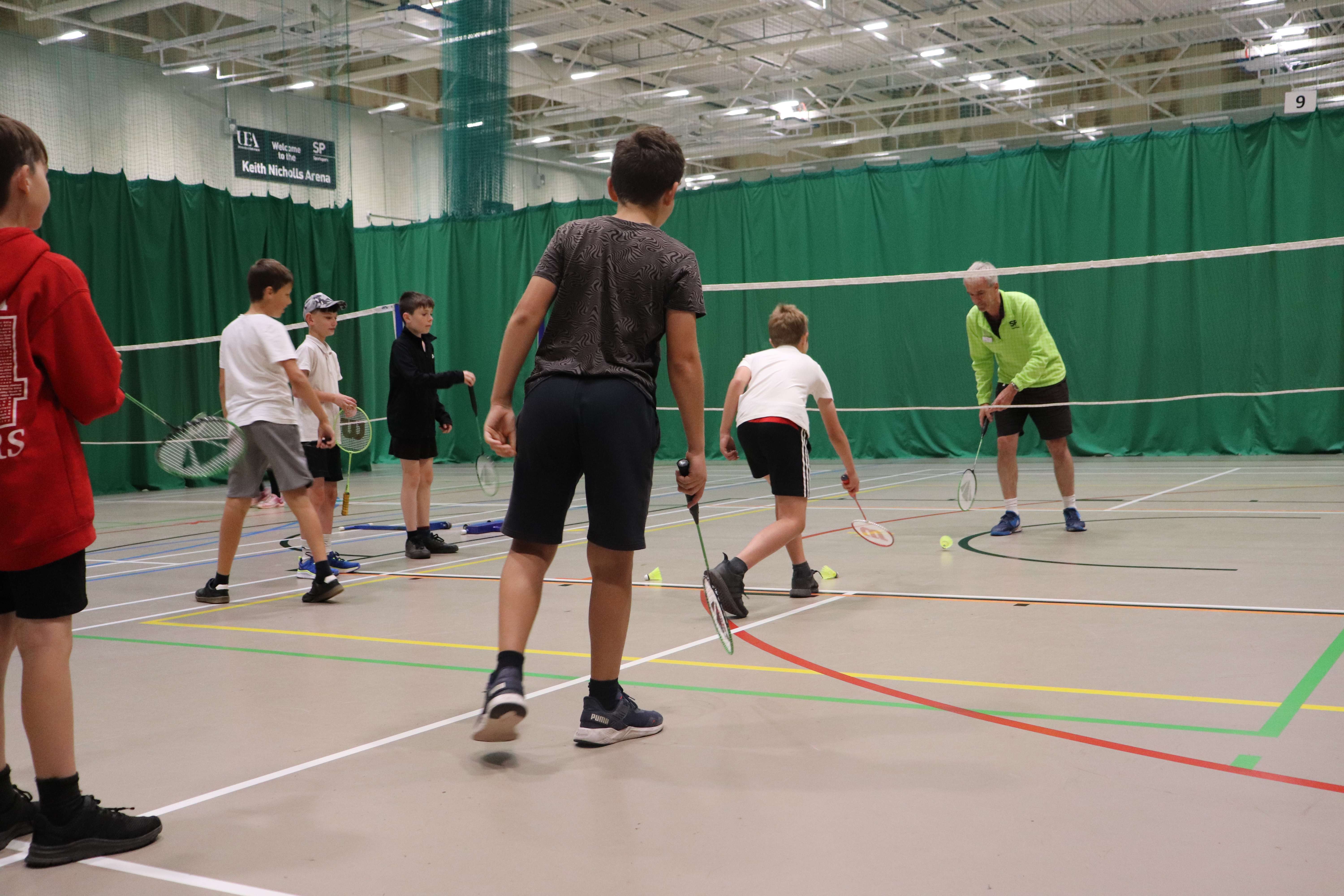 Three children lining up to play badminton with Sportspark coach.