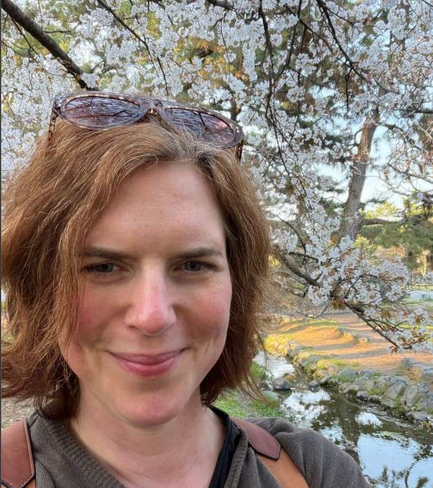 A woman s=with short brown hair in front of a blossom tree