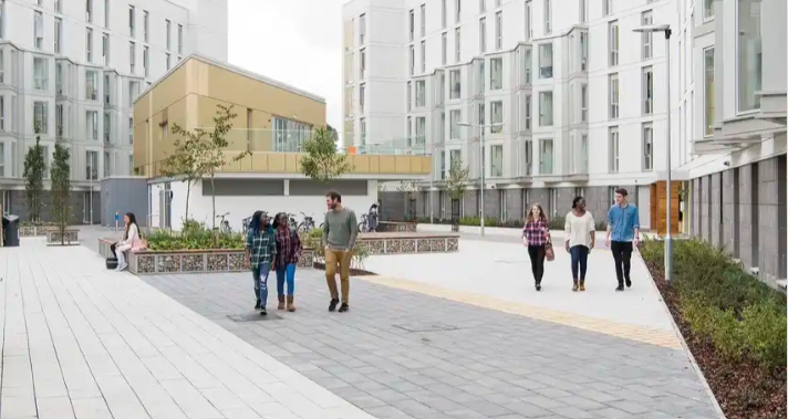 Students walk through a modern courtyard between large, white student accommodation buildings on a university campus.