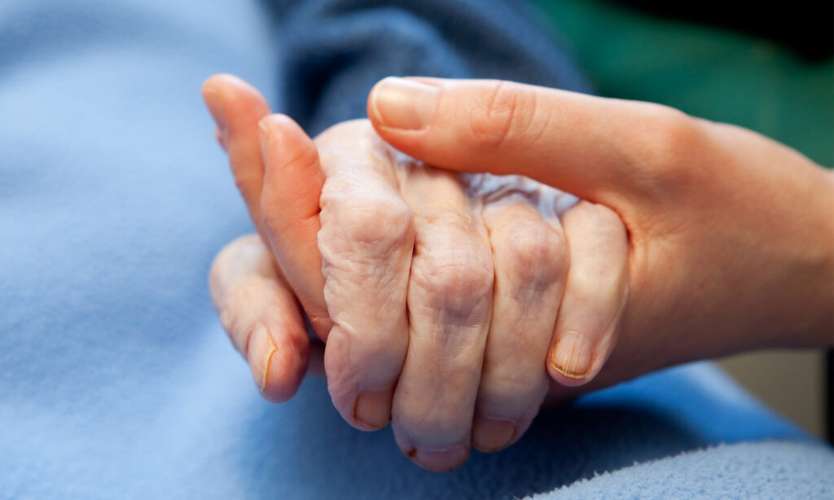 Two people, one depicting and elderly person, holding hands