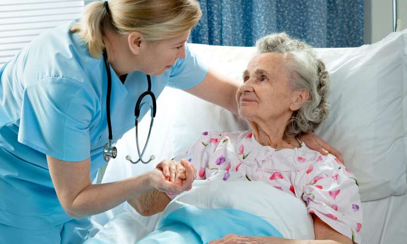 Lady in care bed holding the hand of a healthcare worker