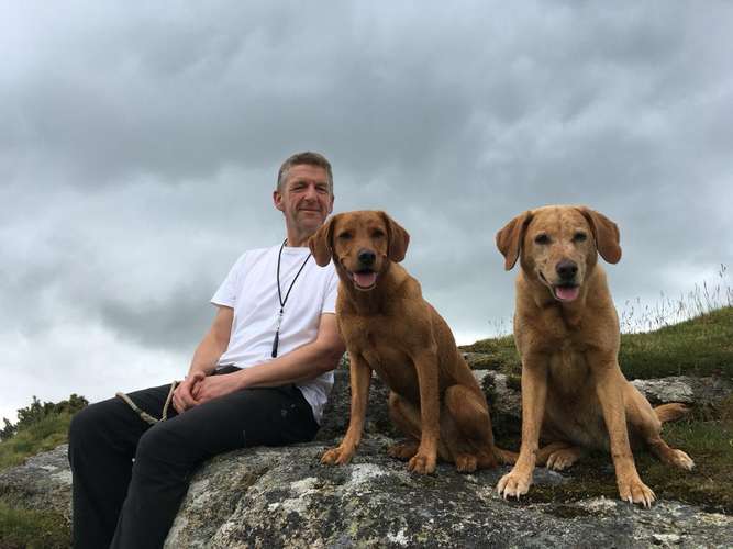 Man sitting with two golden Labrador dogs