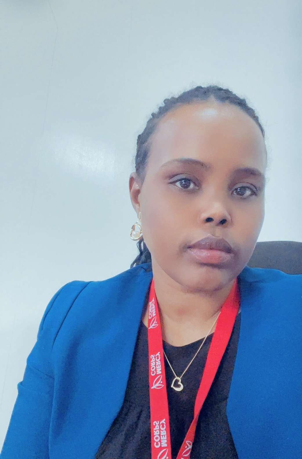 Person wearing a blue blazer and red lanyard, seated against a light background, looking at the camera with a neutral expression.