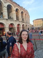 Woman with brunette hair wearing a read blouse and sunglasses on head smiling in front of colosseum