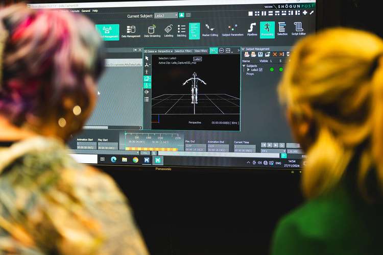 Two people observe a computer screen displaying motion capture software with a skeletal figure and various control panels.