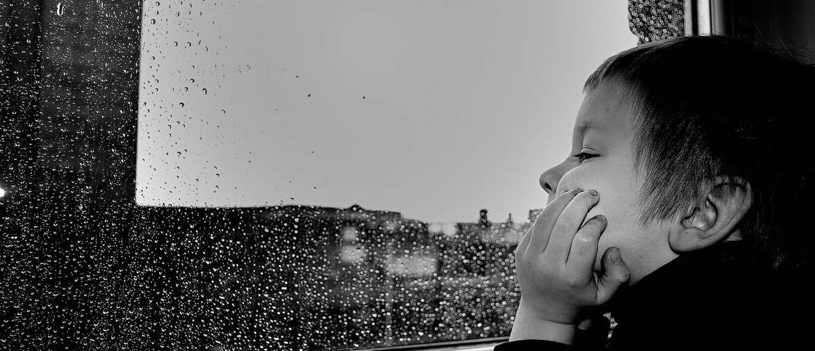 Child looking out out of a window, watching the rainfall.