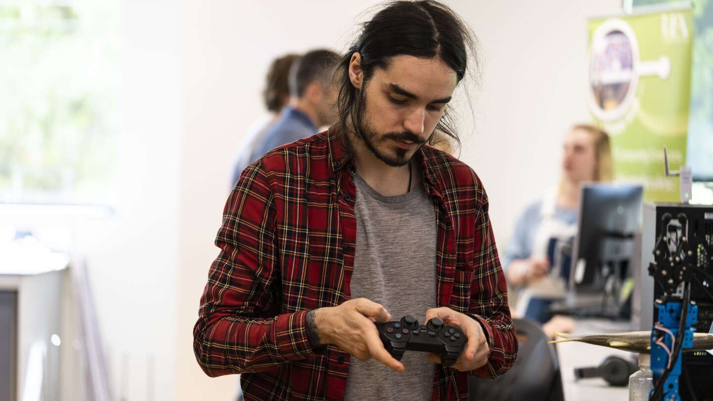 A student in a plaid shirt focuses on a game controller, testing interactive technology in a Norwich university computer lab.