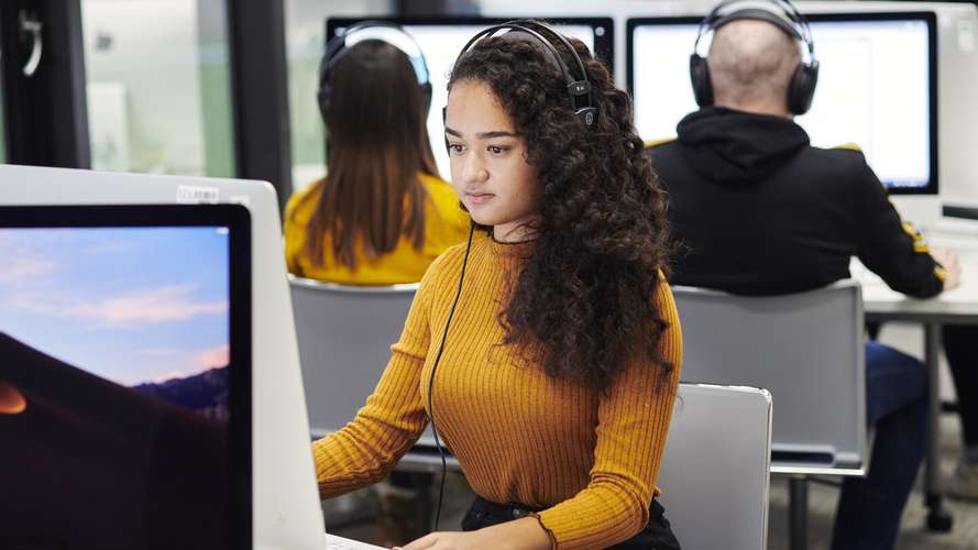 Student in media lab on computer with headphones