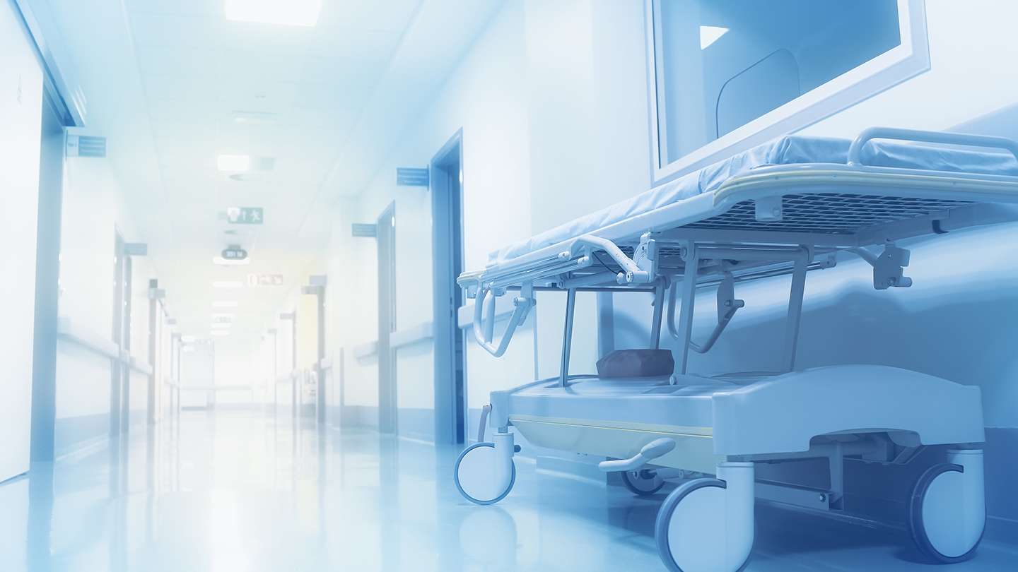 A corridor in a hospital with an empty bed at the side