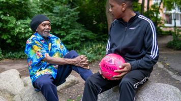 Two people sitting on rocks, one person is holding a pink football