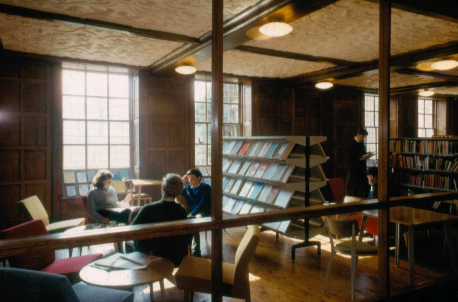 Looking at three students having conversations on chairs in the Earlham Hall library through a panel window
