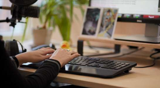 Somebody types on a keyboard. Artwork can be seen in front of the screen.