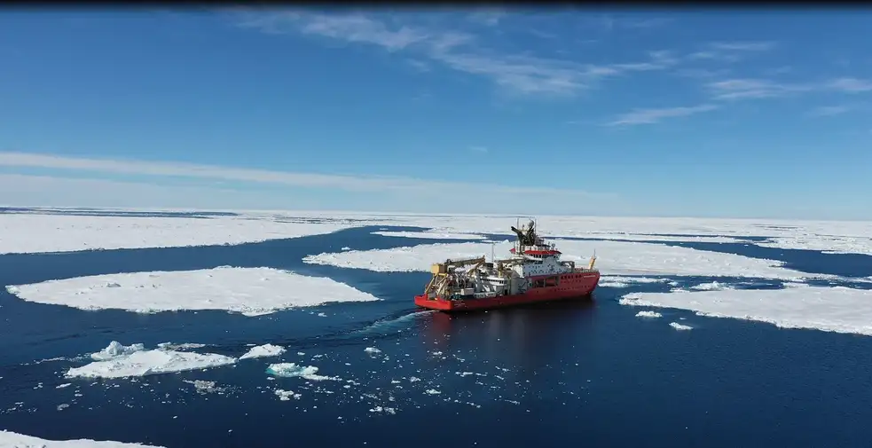 A red research vessel sails through icy waters in the Antarctic Ocean.