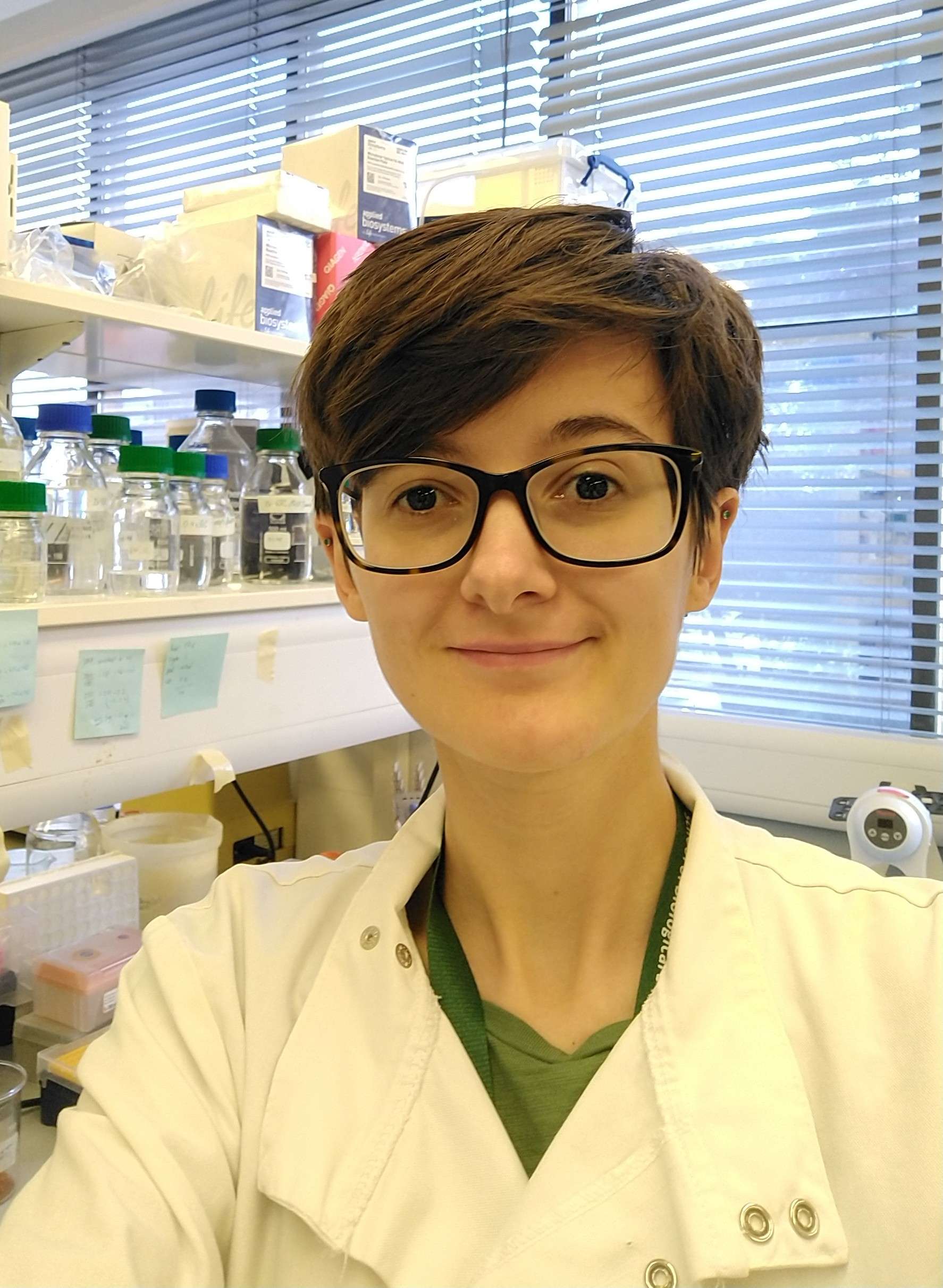 A researcher in a lab smiles at the camera.