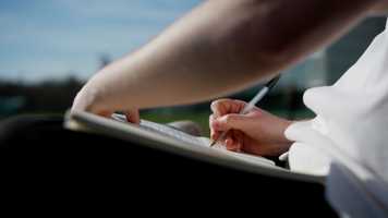 Someone writes in a book outside.