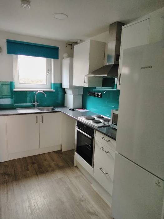 kitchen with white cabinets, teal backsplash, electric stove, sink, and large fridge. Window with teal blind lets in natural light.