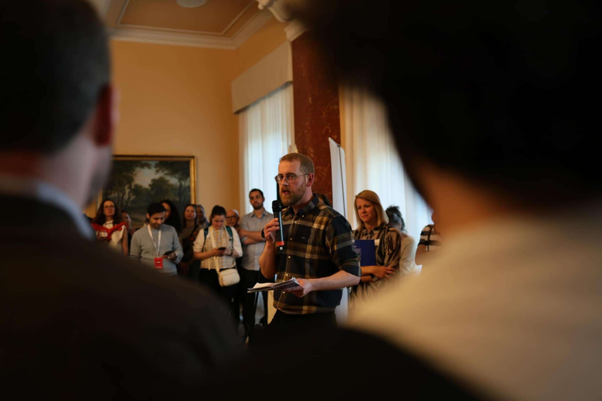 A male presenter speaking into a microphone to an attentive audience