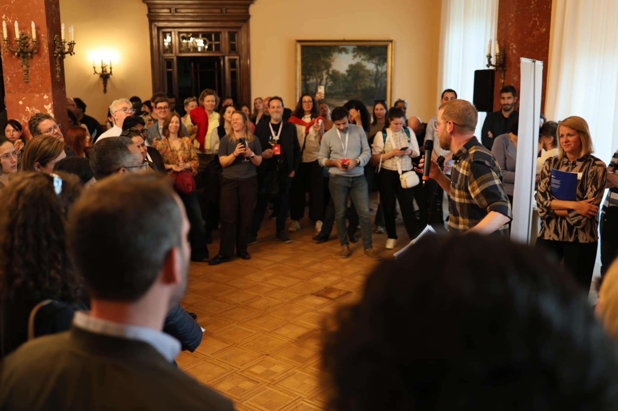 A presenter chats to an engaged audience of people held in an elegant hall.