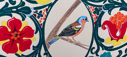 Colorful bird illustration within an ornate floral border, featuring red, yellow, and blue flowers with green leaves.