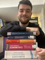 Smiling man leaning on a stack of econometrics and time‑series textbooks, including the Palgrave Handbook of Econometrics.