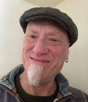 Smiling man with blue eyes, grey beard, earring, wearing a farmer's hat