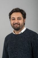 Smiling man with beard and grey jumper against grey background