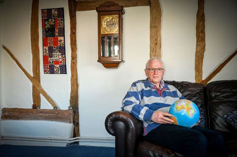 Person sat on a sofa holding a globe, with a clock behind them