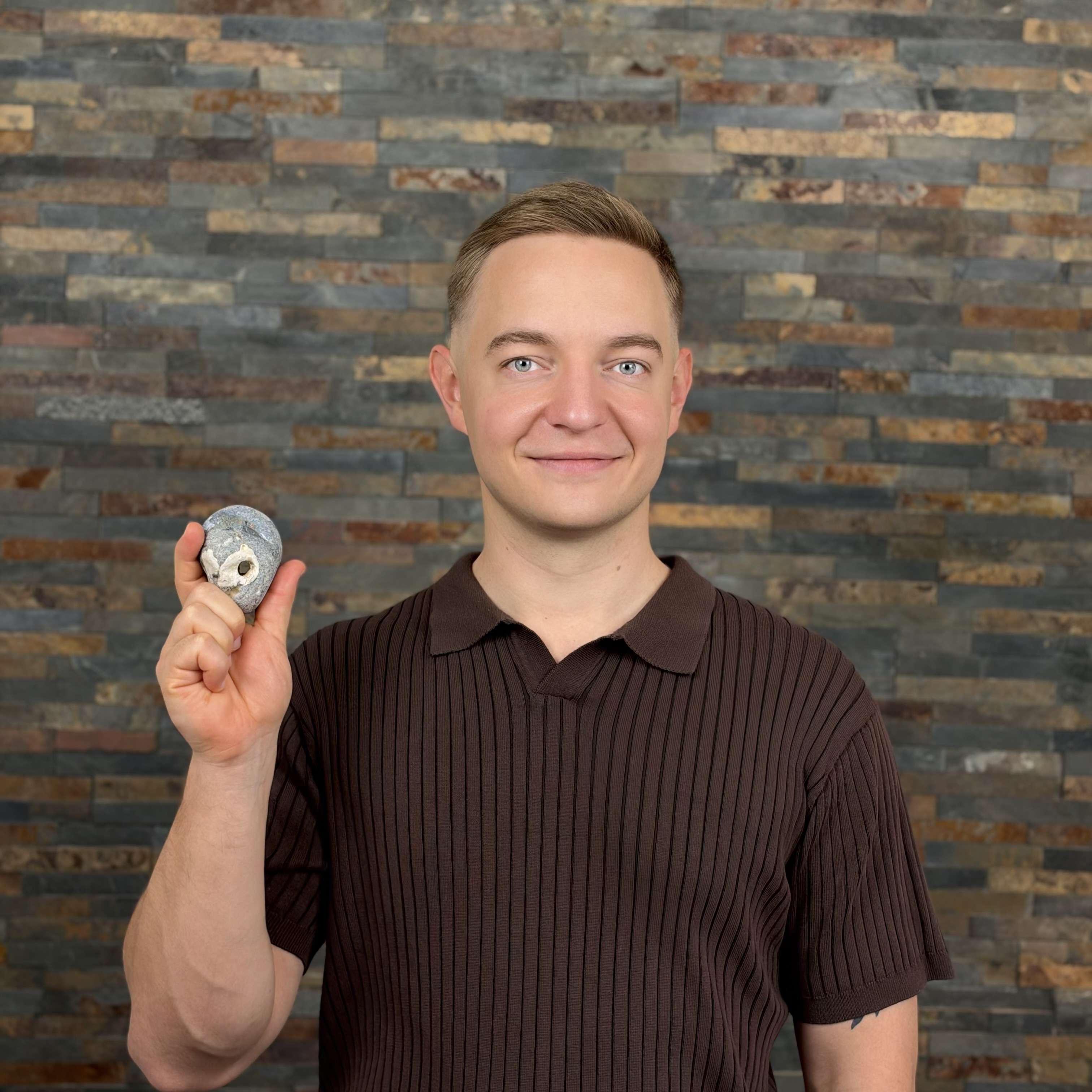 A person holding a small rock smiles at the camera.