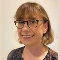 A person with short brown hair and glasses smiles, wearing a patterned top against a plain background.