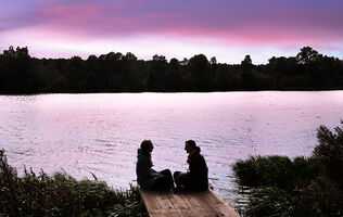 Two people sitting by a lake at sunset