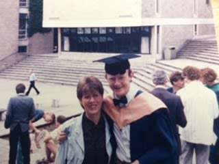 Person in graduation gown with another person, in the UEA Sqaure