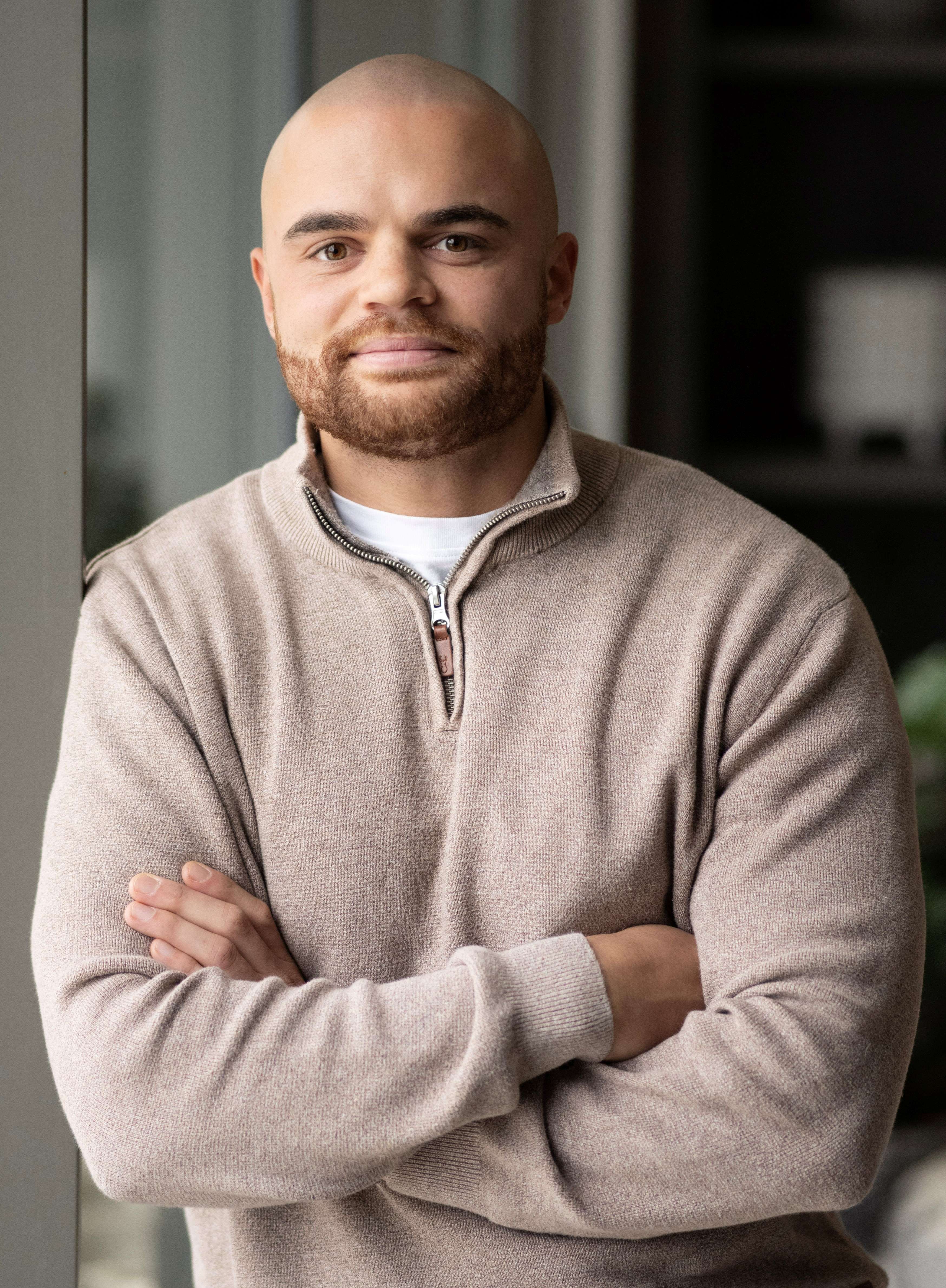 A portrait photo of someone looking at the camera with their arms crossed.