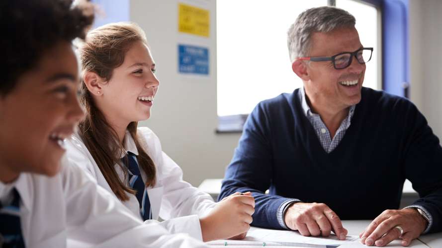 Male High School Tutor Sitting At Table With Students Teaching Lesson