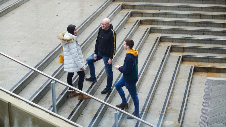 Mature students standing and walking outside in the autumn, talking and socialising.