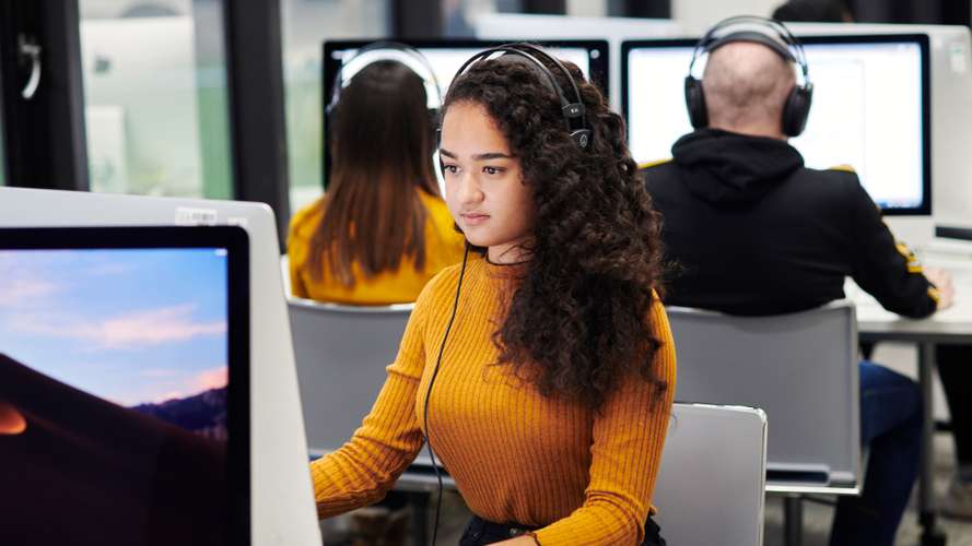 Mature student in media lab on computer with headphones.