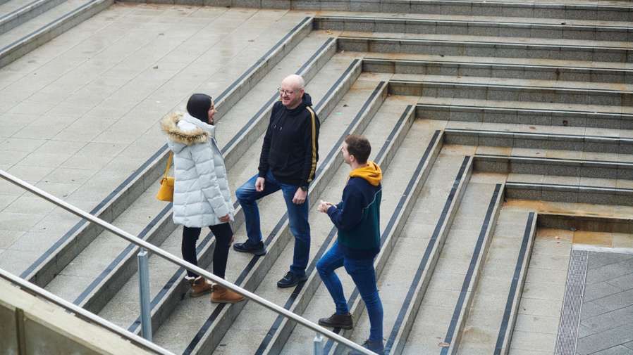 Mature students standing and walking outside in the autumn, talking and socialising.