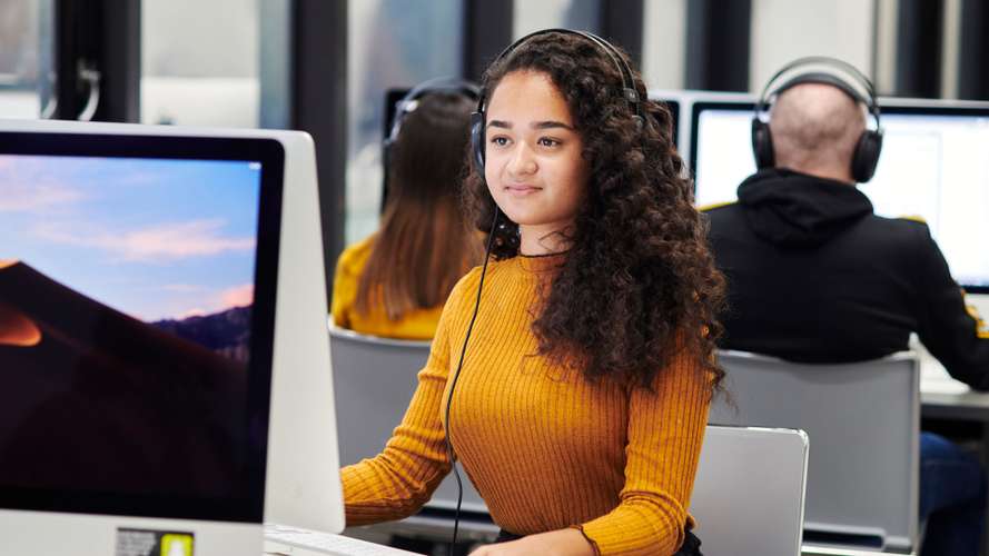 Mature student in media lab on computer with headphones.