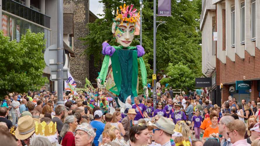 Image of a crowded street in Norwich with a large puppet in the middle distance looming over the crowd