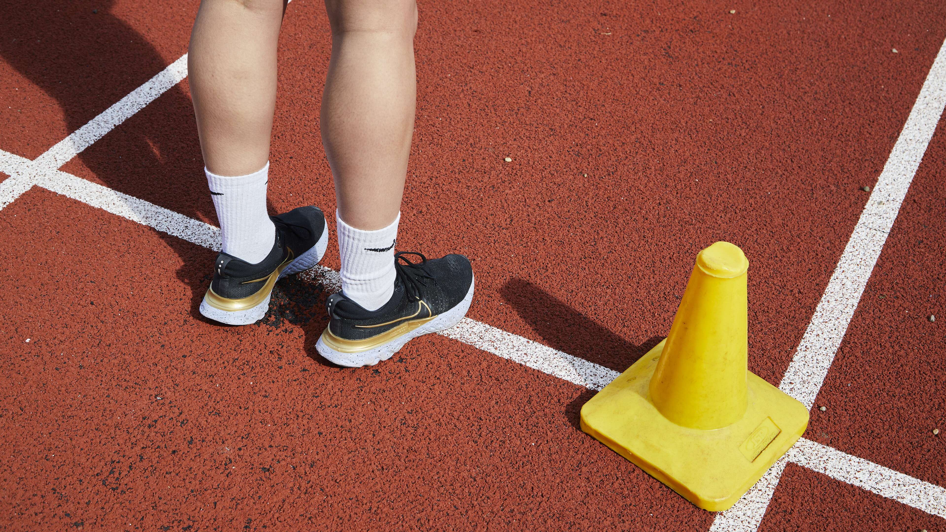 A student stands on a red athletics track next to a yellow cone, highlighting sports science research and courses.