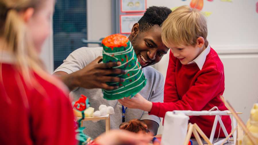 Young teacher is helping one of his primary school students during arts and crafts lesson.