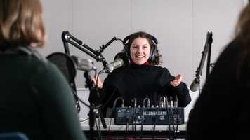 A student wearing headphones speaking into a microphone in a studio setup
