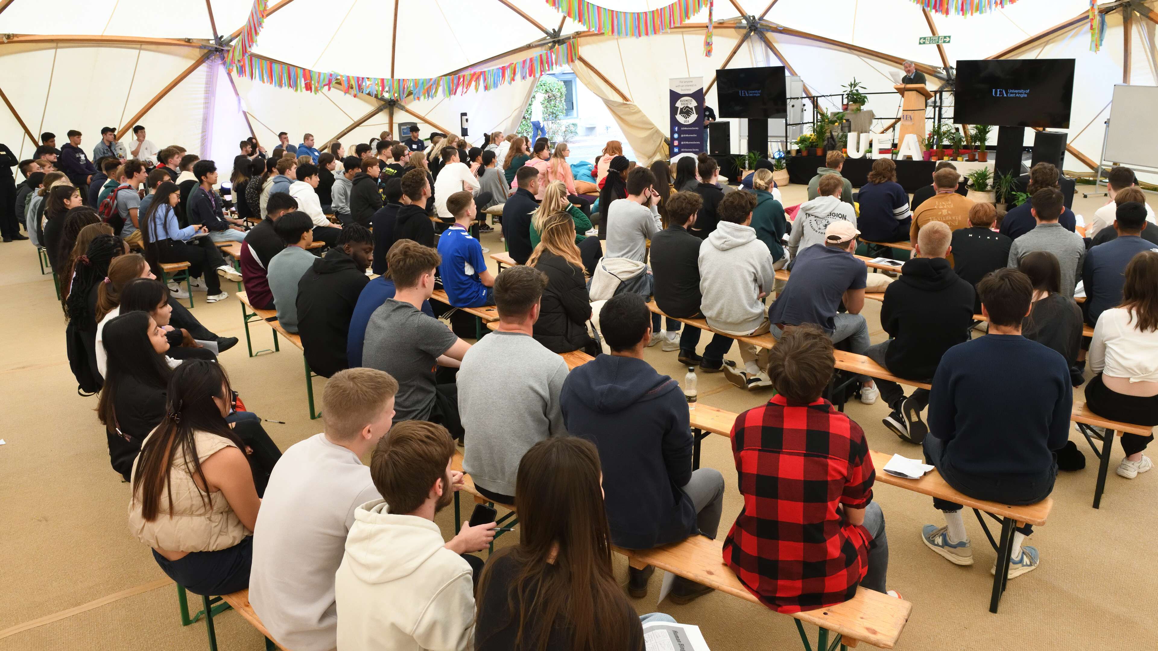 A room of students listening to someone speak on stage.