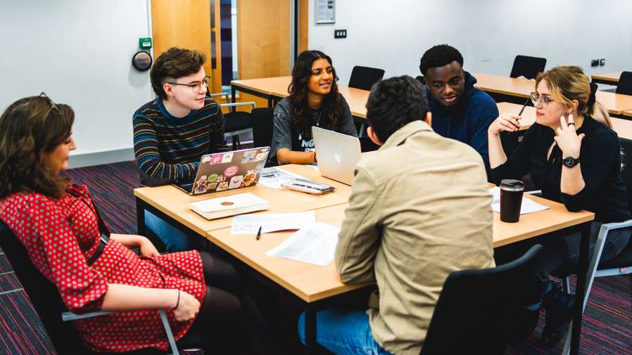 Group of students in a seminar room having a discussion around a table
