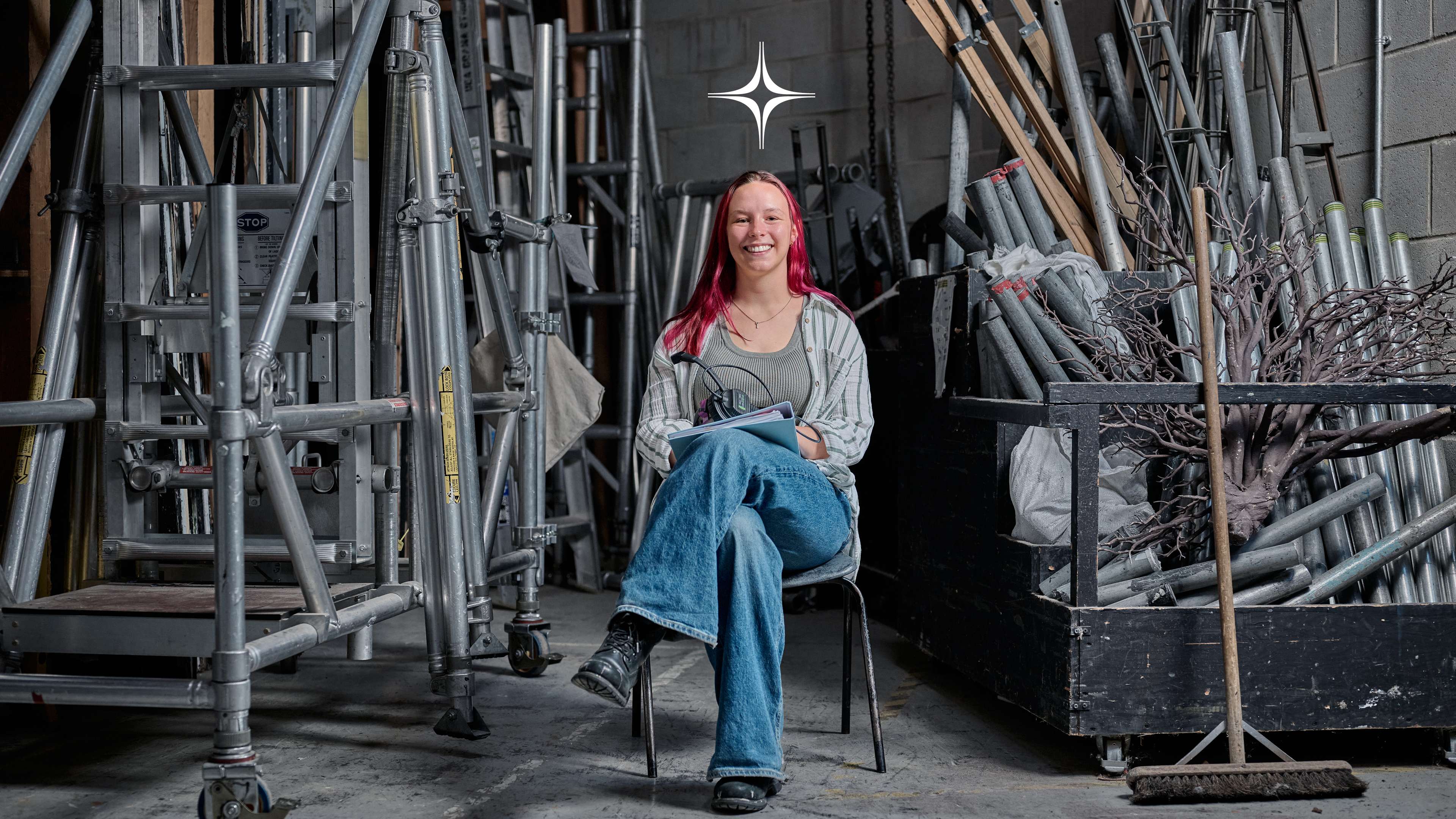 A student sits on a chair surrounded by theatre equipment.