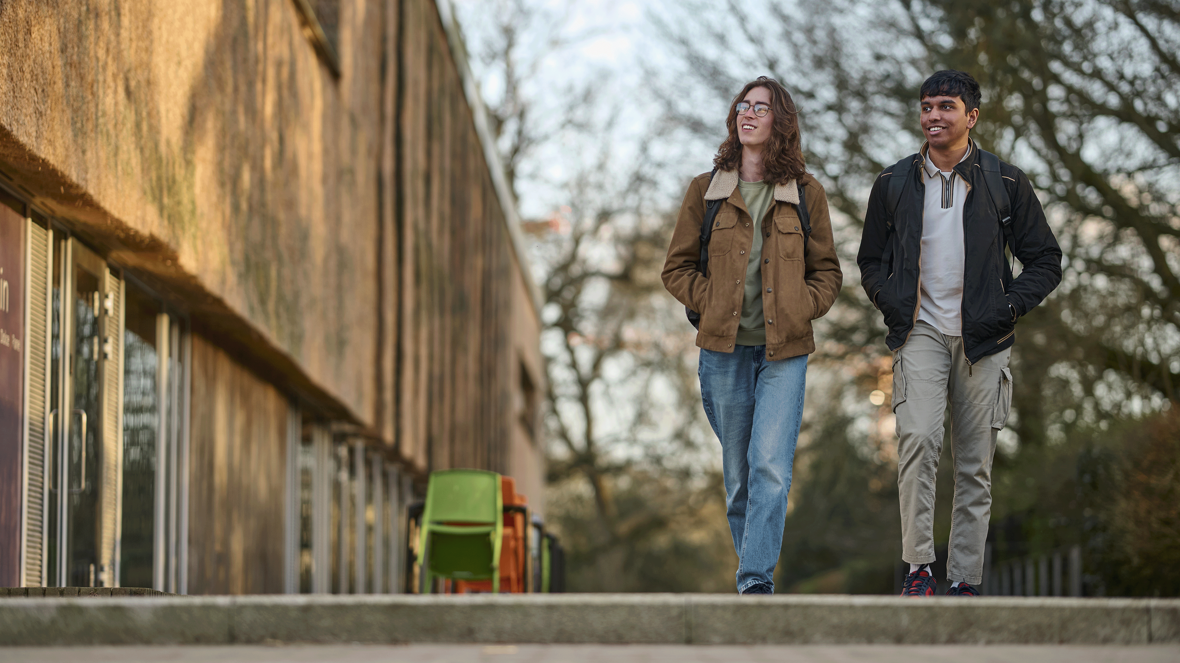Two smiling students walk along a path outside a building.