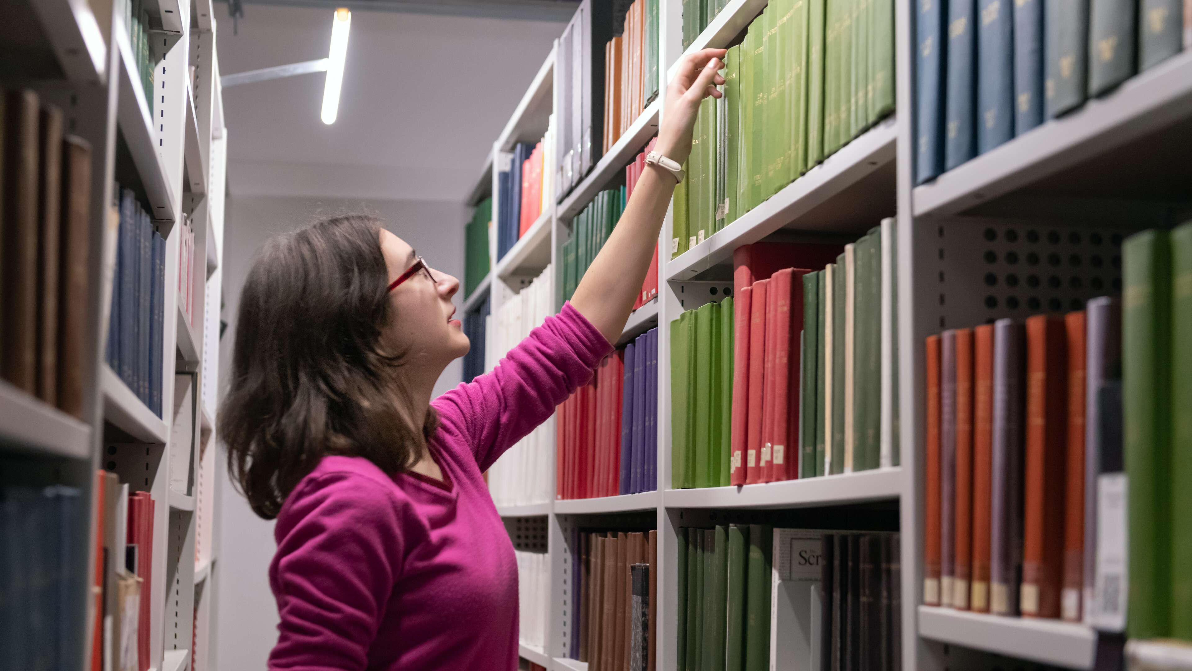 Woman reaching for a book on a library shelf
